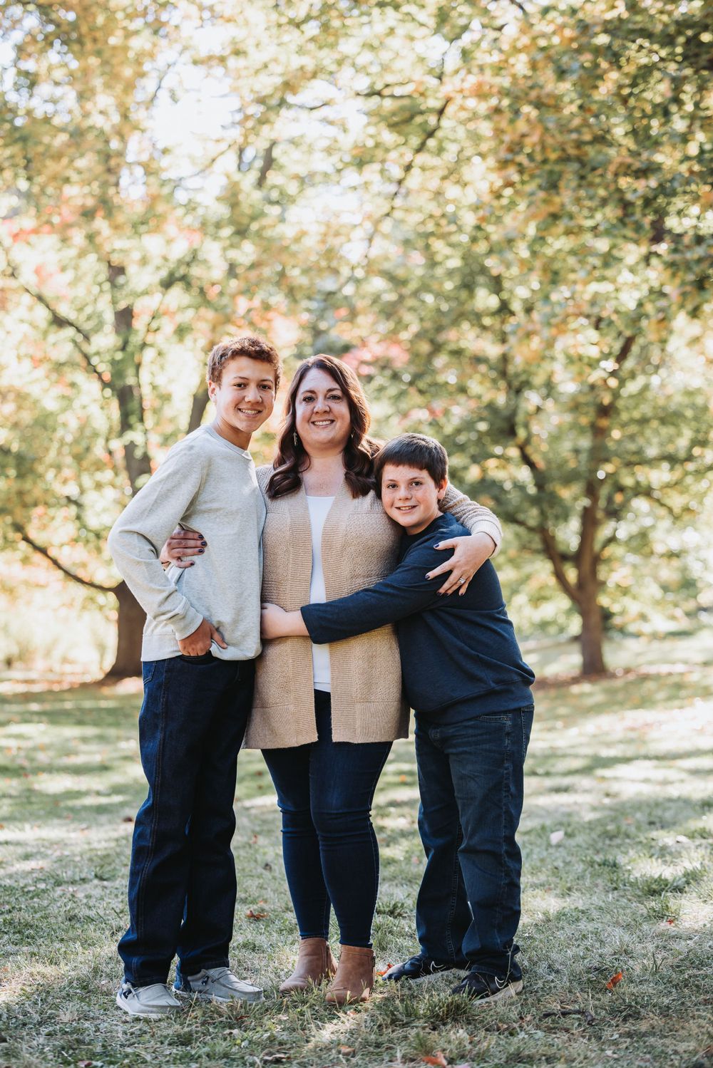 A happy family stands in a grassy field with trees behind them, enjoying their time together during a family session in Finch Arboretum