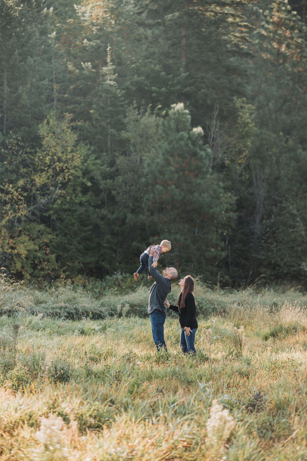 A family poses together in a field, surrounded by trees, capturing a joyful moment during their family session.