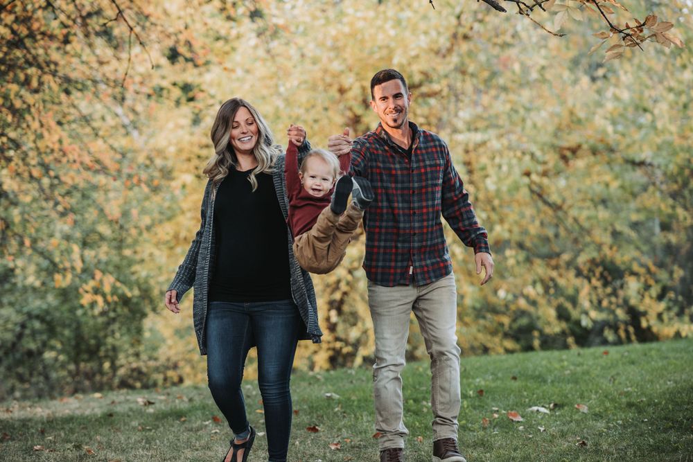 A happy family stands in a grassy field with trees behind them, enjoying their time together during a family session in Finch Arboretum