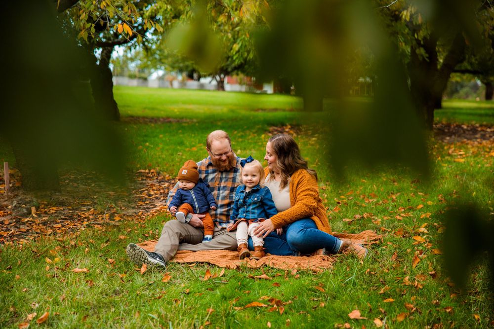 A family enjoying a sunny day sitting on the grass under a tree in Manito Park.