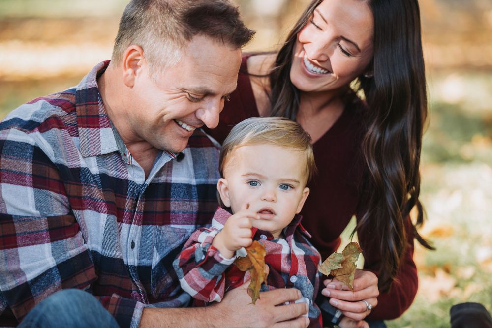 A happy family sits in a grassy field with trees behind them, enjoying their time together during a family session in Finch Arboretum