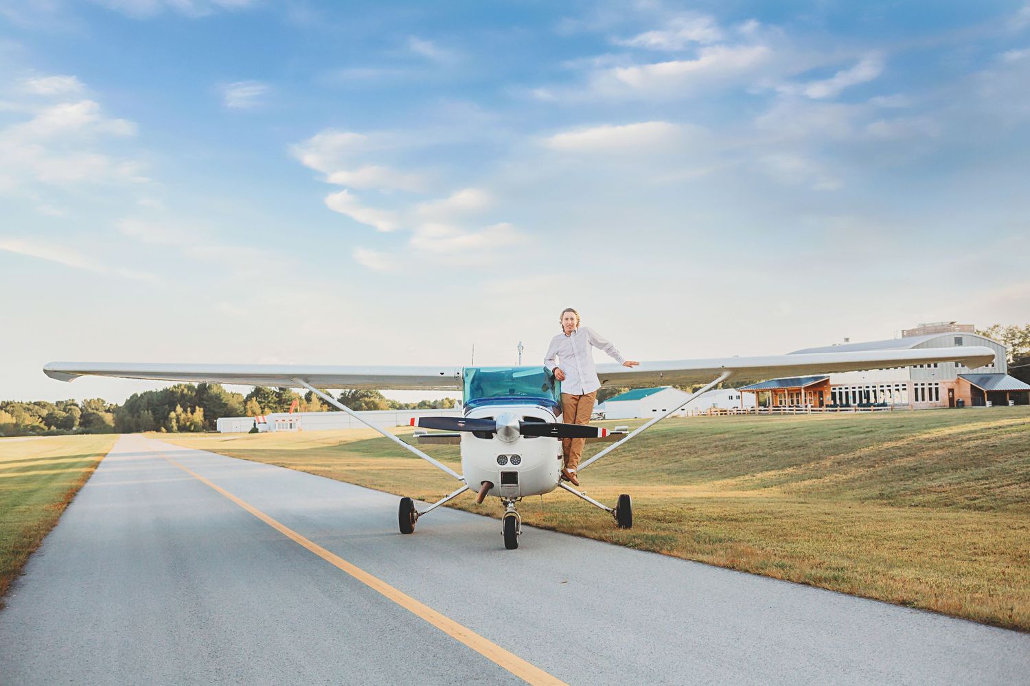 Person standing in front of small private aircraft on runway with clear blue sky.
