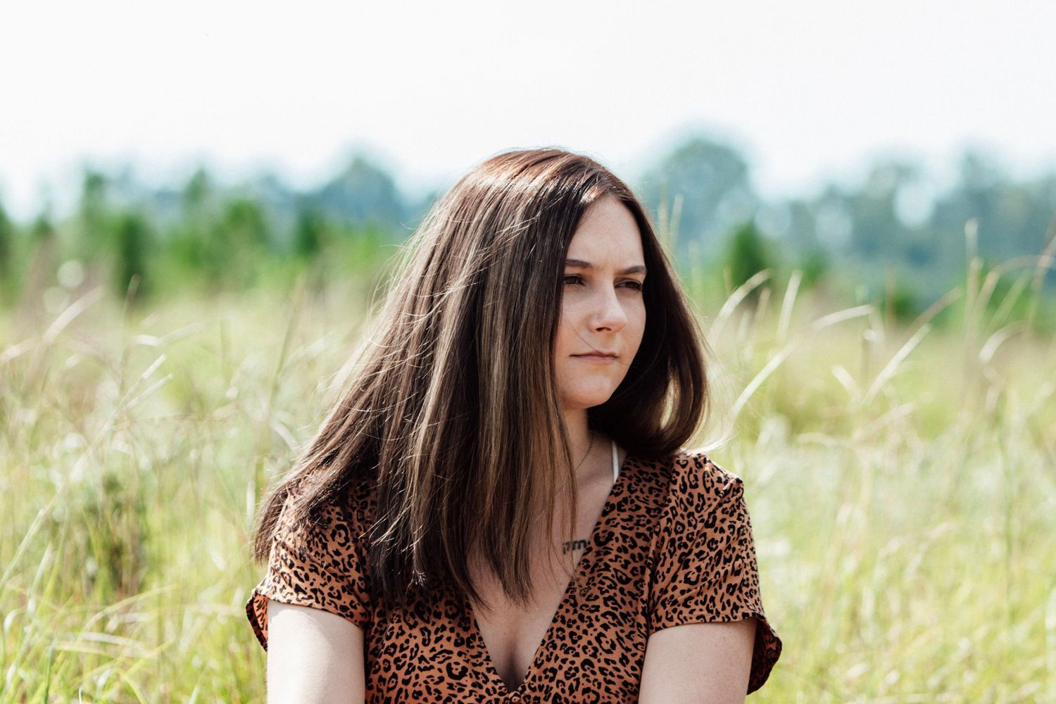 Woman in leopard print dress sitting in tall grass field at sunset.