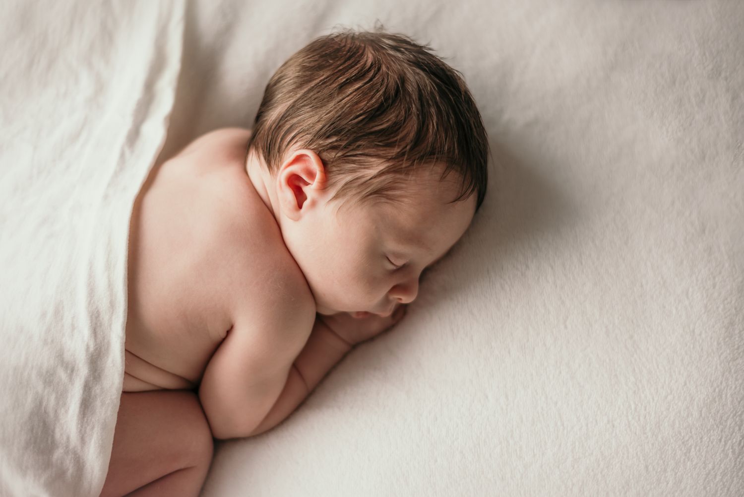 Newborn baby sleeping peacefully on white bedding during portrait shoot.
