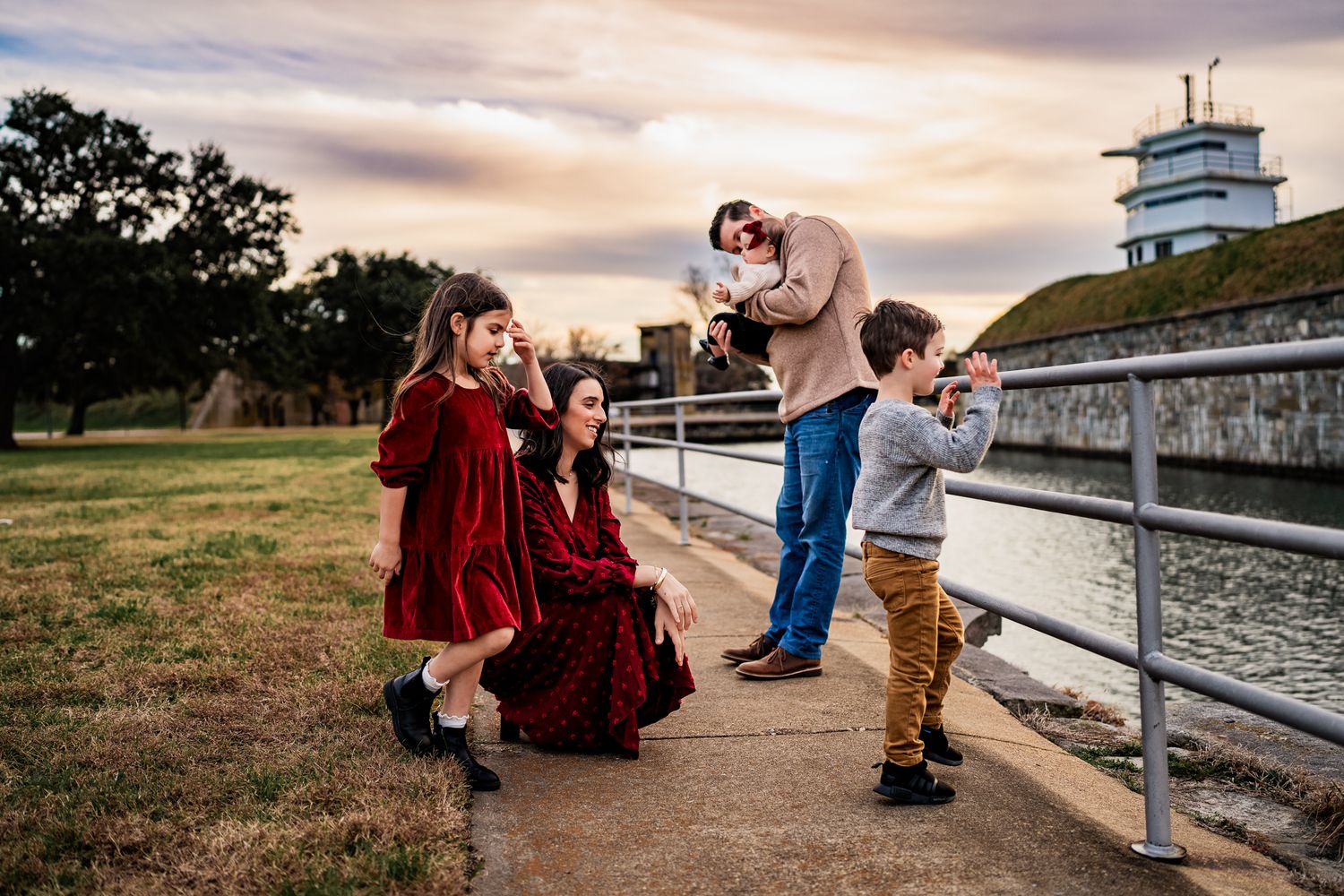 A playful family moment captured at sunset near a historic lighthouse.