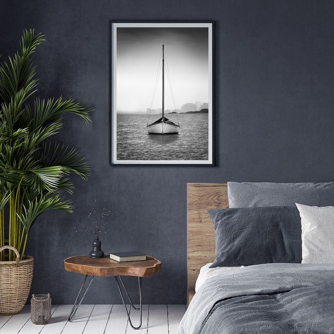 Black and white photograph of a sailboat anchored in calm waters displayed in a bedroom with modern decor.