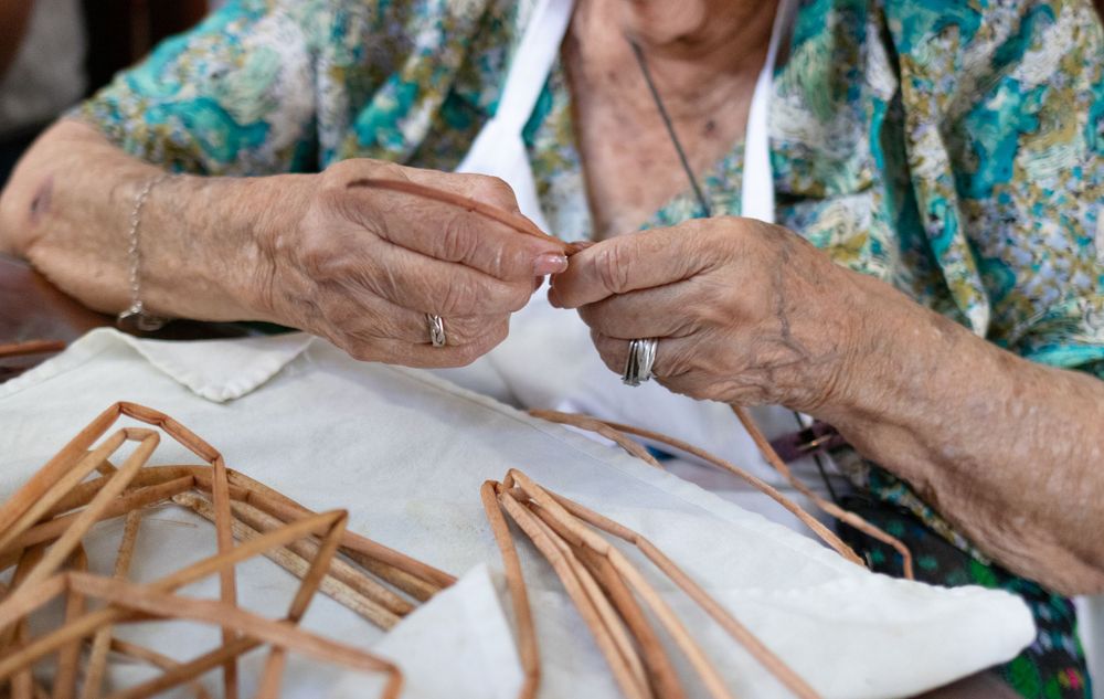 Hands wrapping traditional tamales in corn husks on a white surface.