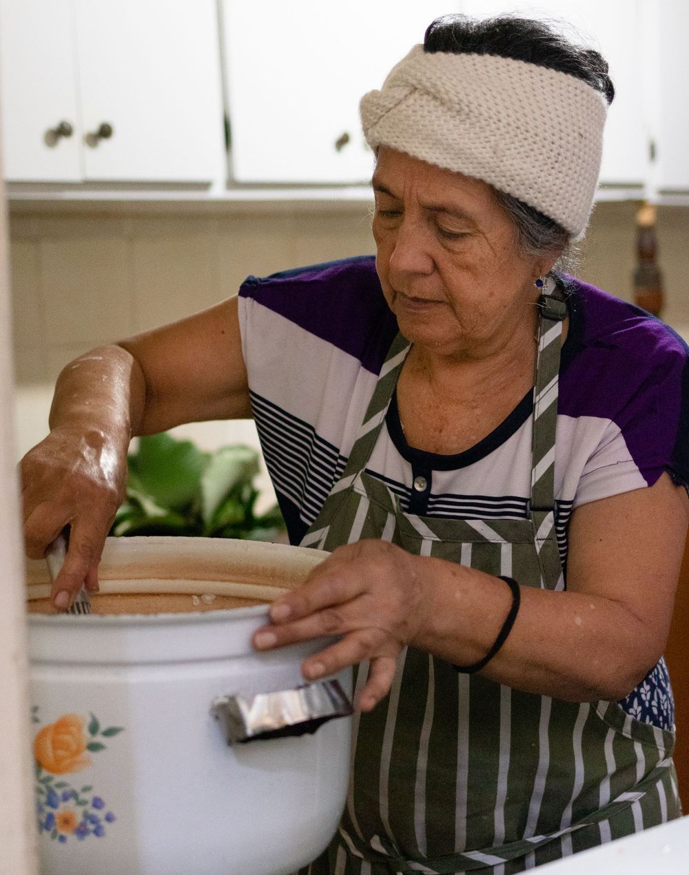 Kitchen workers in striped aprons and white hats prepare food together in a commercial kitchen setting.