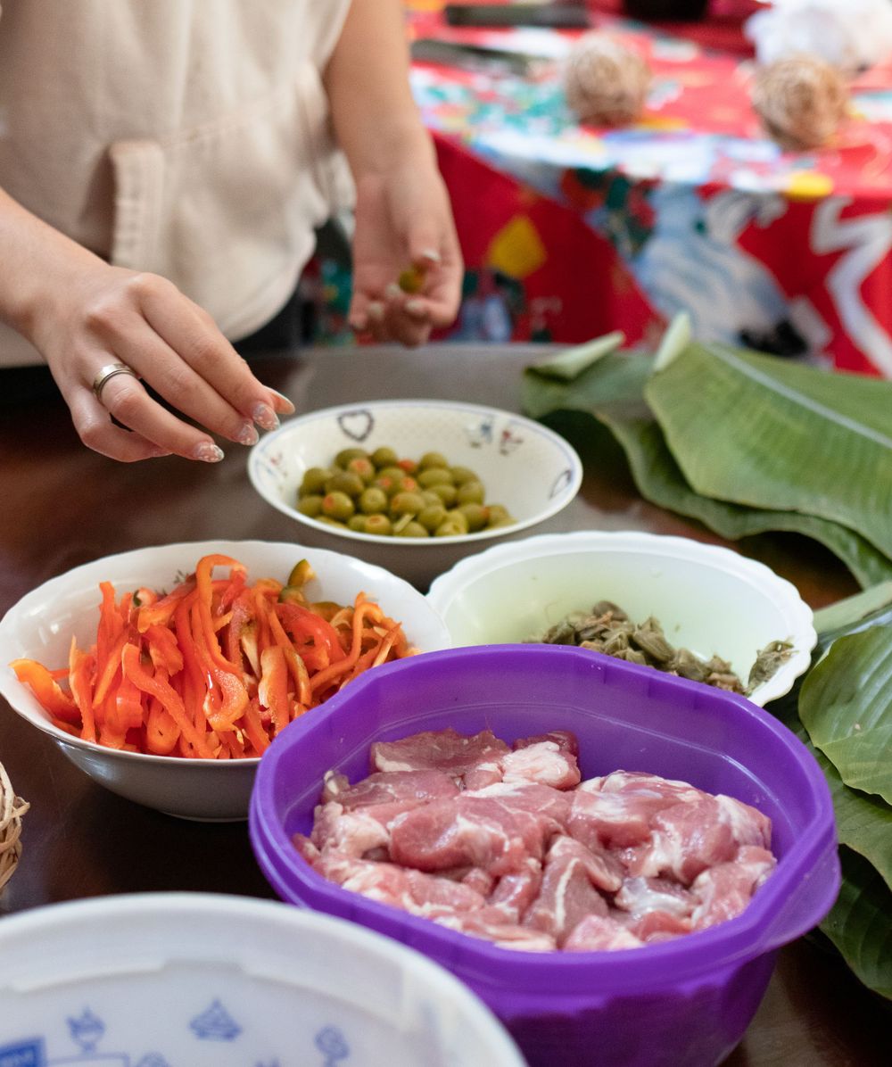 Colorful bowls of prepared ingredients including carrots, meat, and olives arranged on a table.