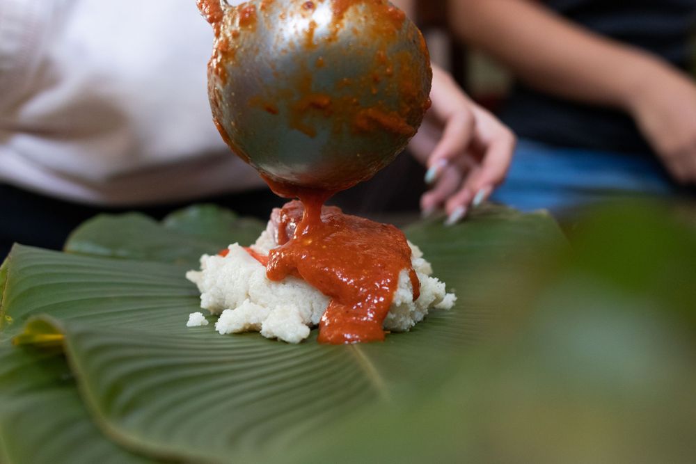 Red sauce being poured over white rice on a green banana leaf.