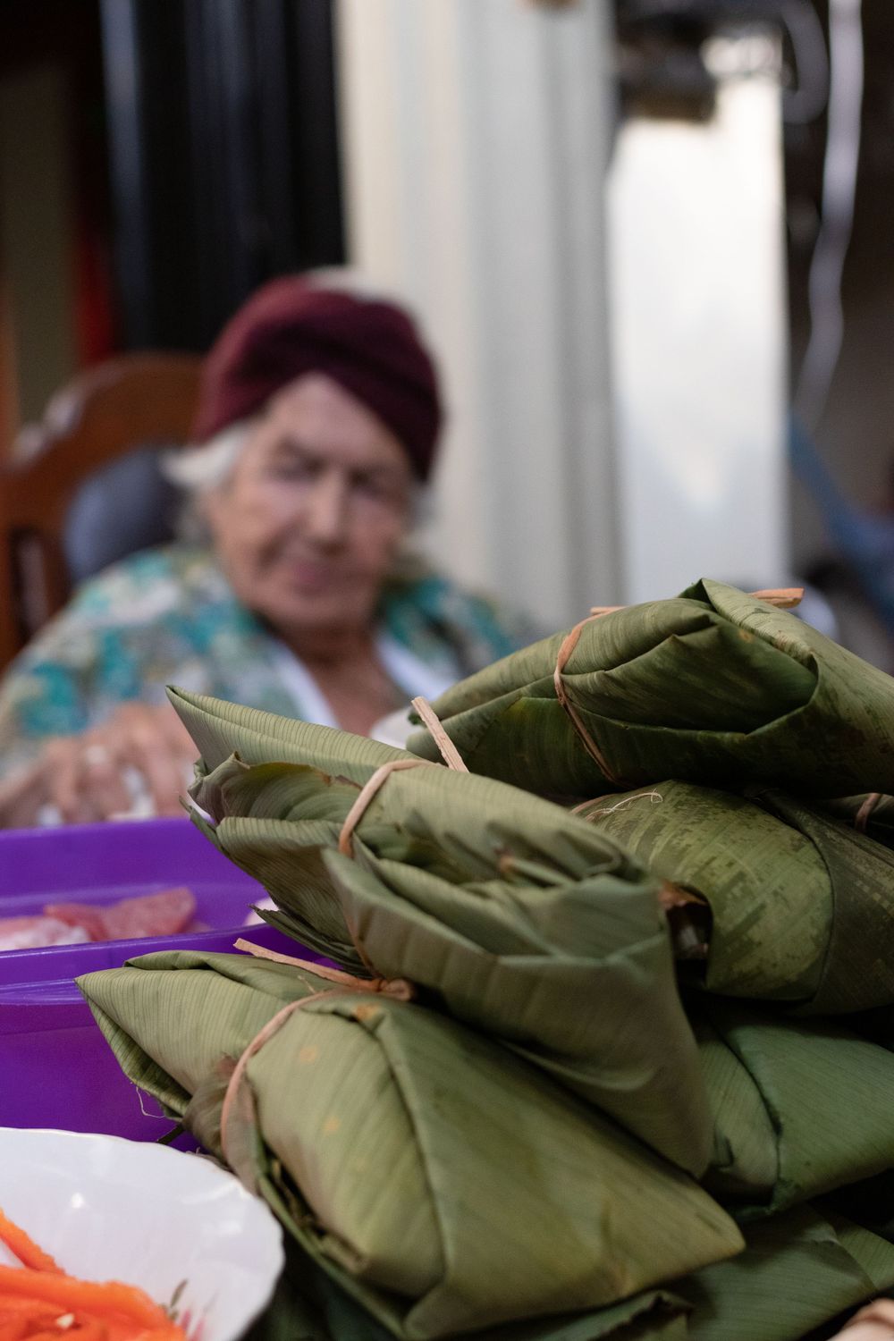 Stack of wrapped green tamales arranged on a purple surface with other ingredients visible.