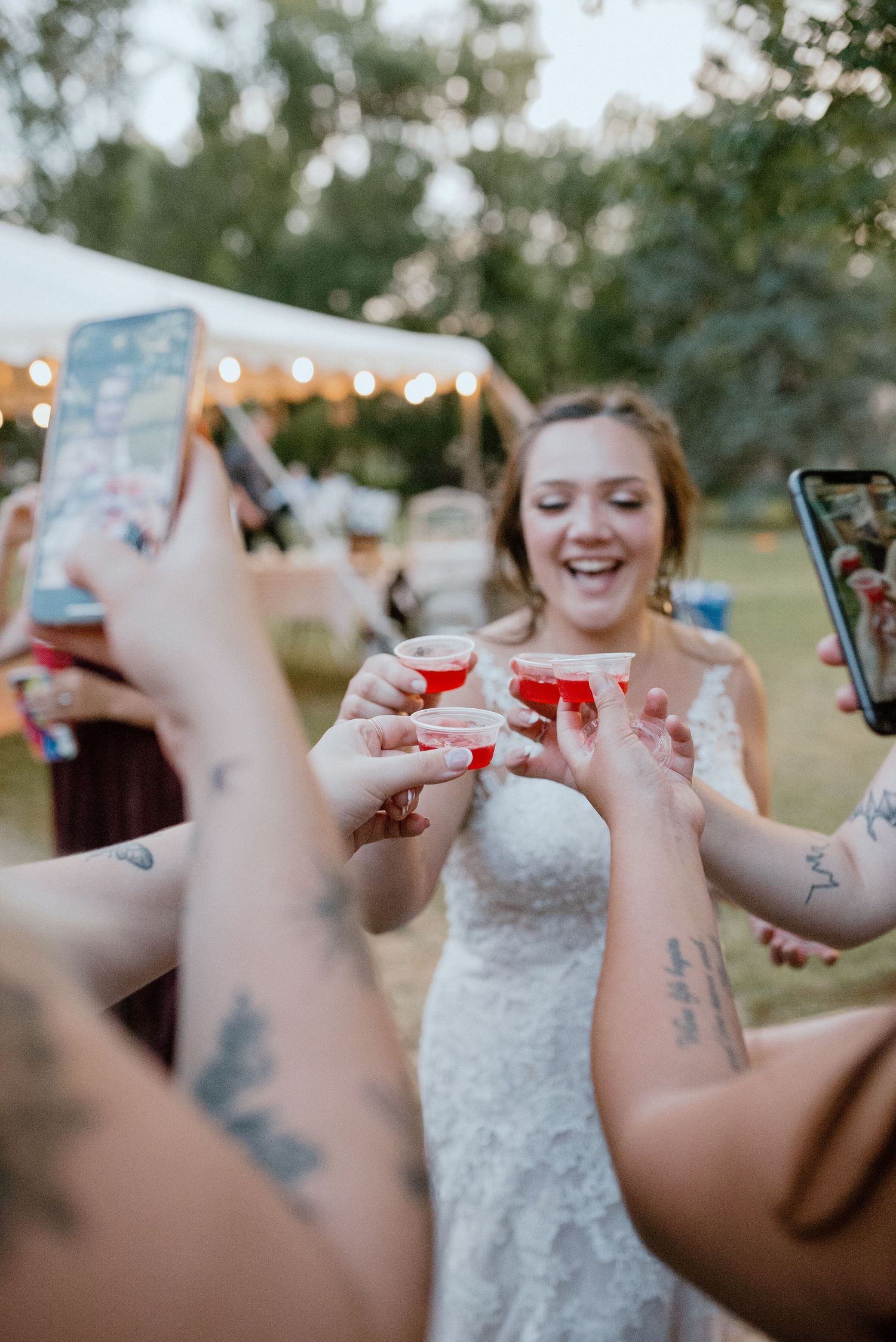 Wedding guests toasting with red drinks under twinkle lights at an outdoor reception.