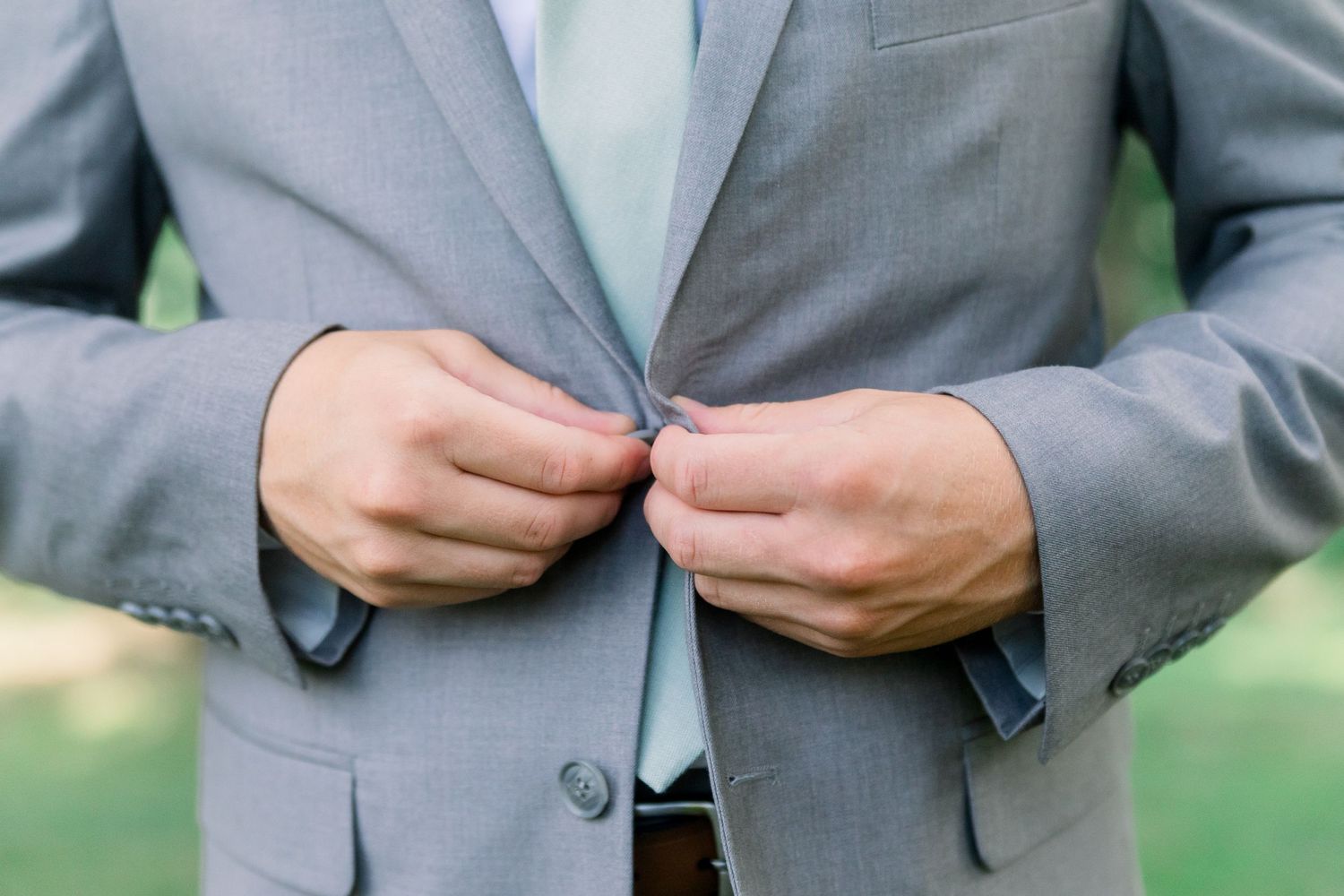 Groomsmen in gray suits adjust their mint green ties while getting ready for a wedding ceremony.