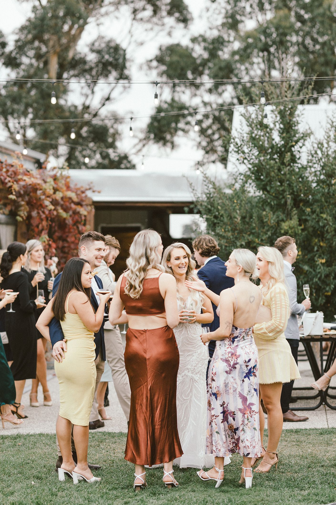 Group of wedding guests in formal attire mingling on a lawn during an outdoor reception.