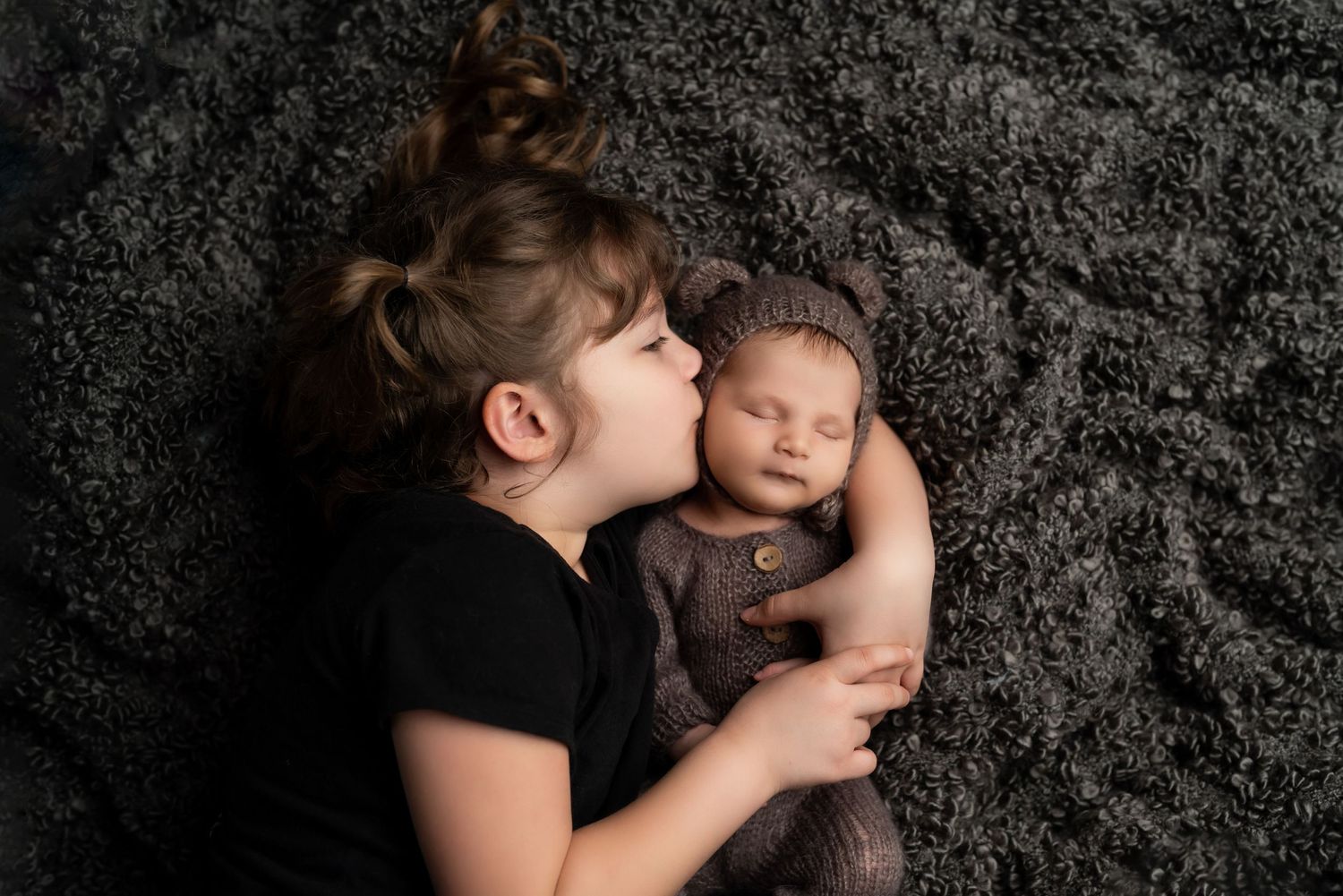Intimate black and white portrait of mother and baby on dark textured background.