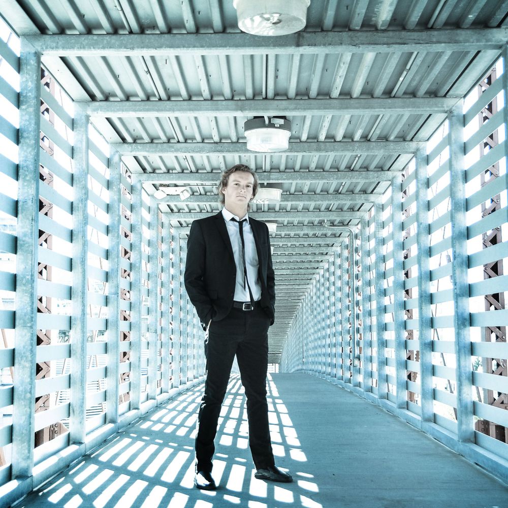 Black-suited figure stands in futuristic corridor with repeating white geometric patterns.