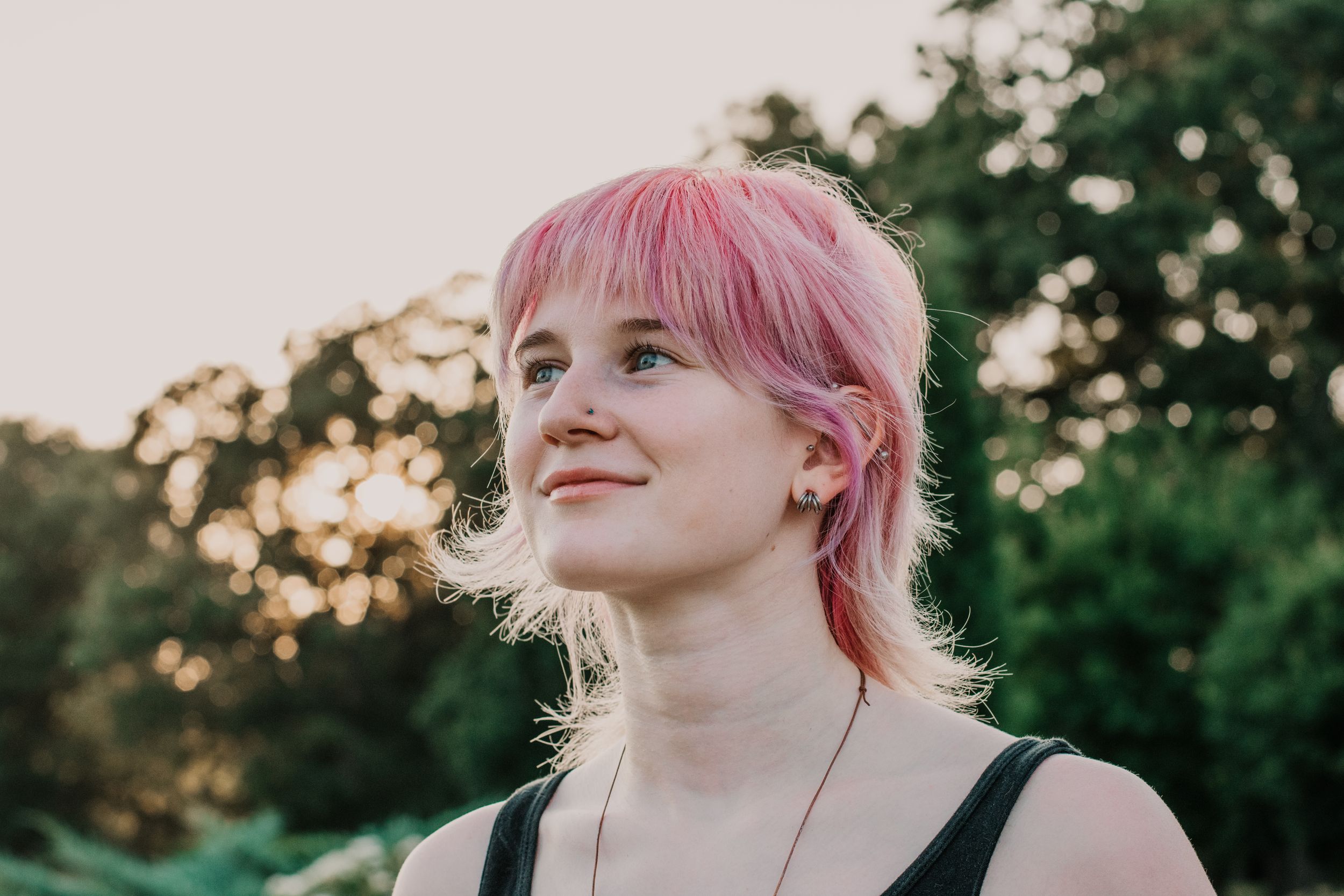 A young woman with pink hair smiles into the setting sun