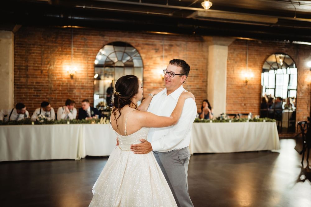First dance in an elegant brick-walled reception space with white table settings.