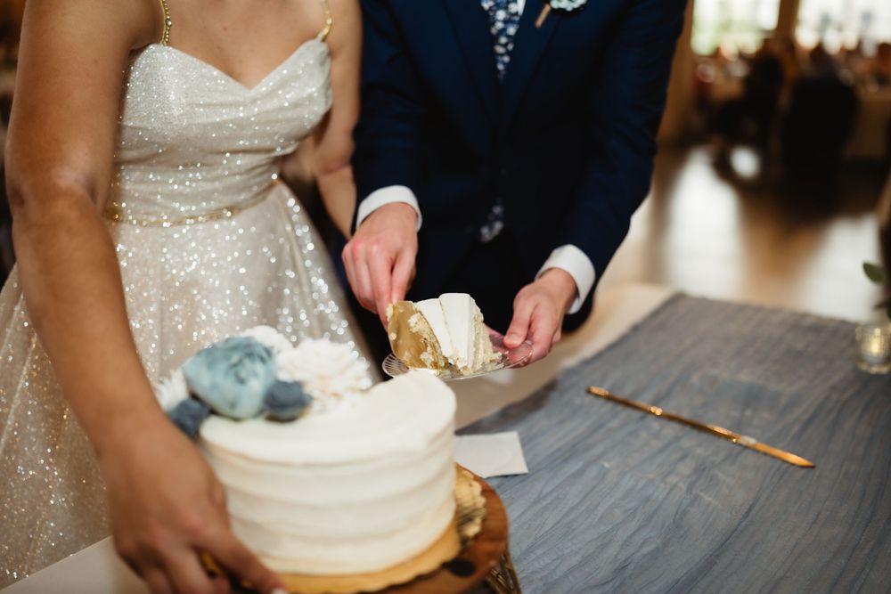Wedding couple cutting into their white tiered wedding cake together.