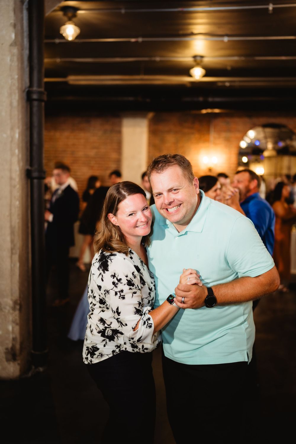 A couple dances together at a wedding reception in a rustic brick venue with industrial lighting.