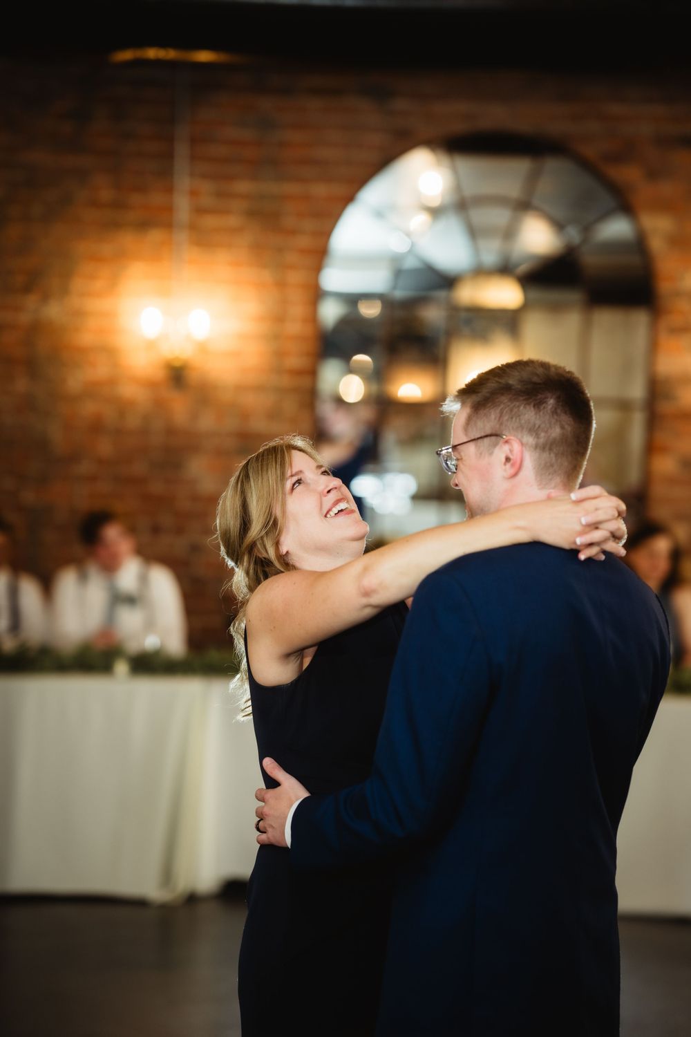 Joyful dance moment in a rustic brick-walled reception venue with warm lighting.