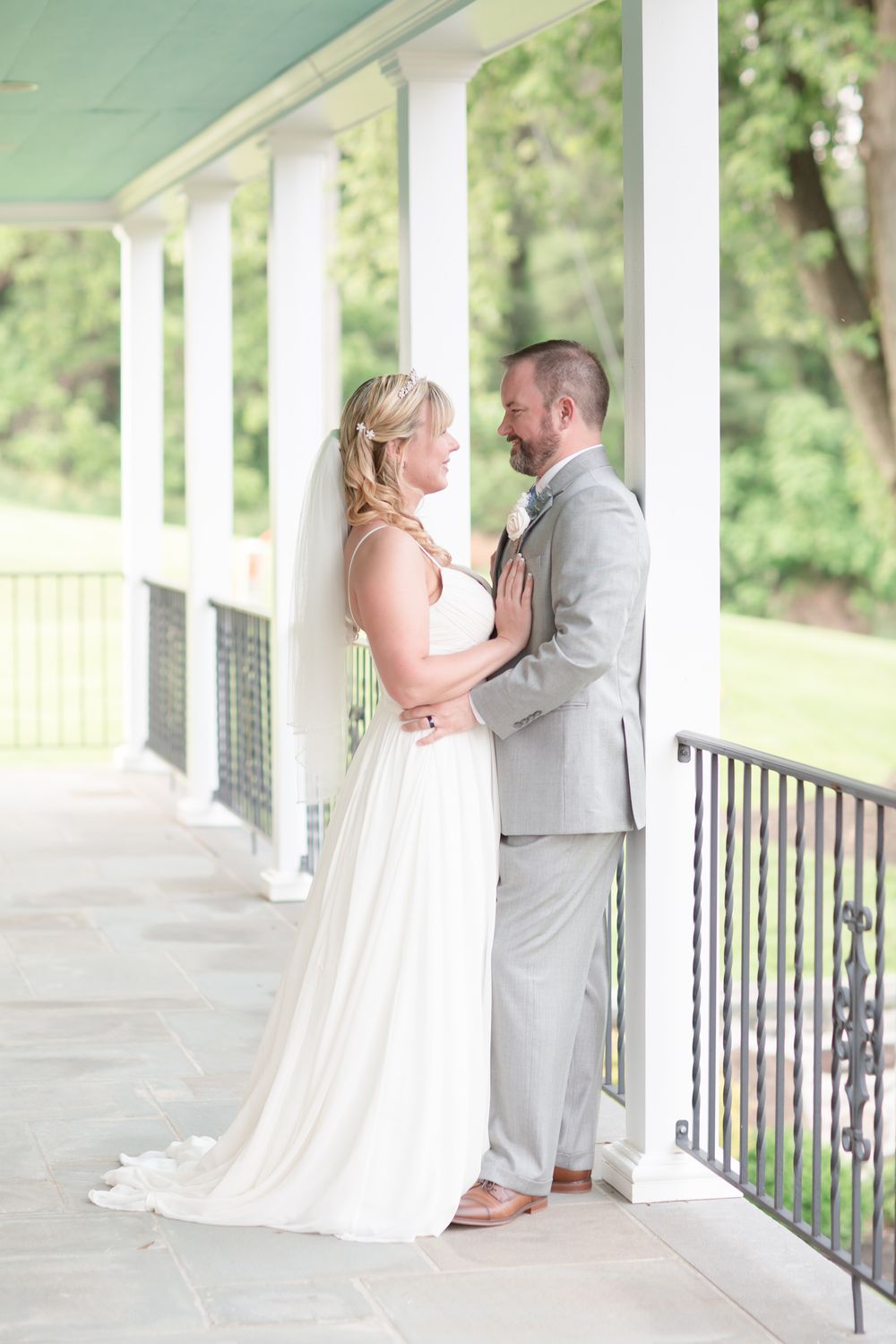 A romantic wedding couple shares an intimate moment on an elegant white-columned porch.
