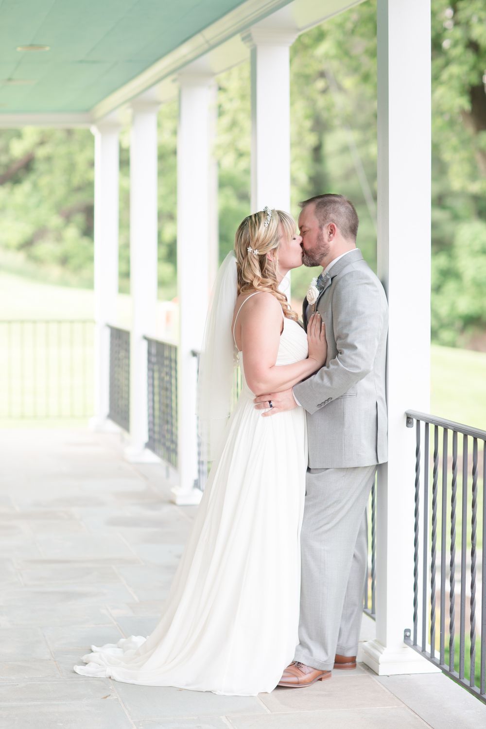 A romantic wedding moment between newlyweds embracing on an elegant covered porch with white columns.