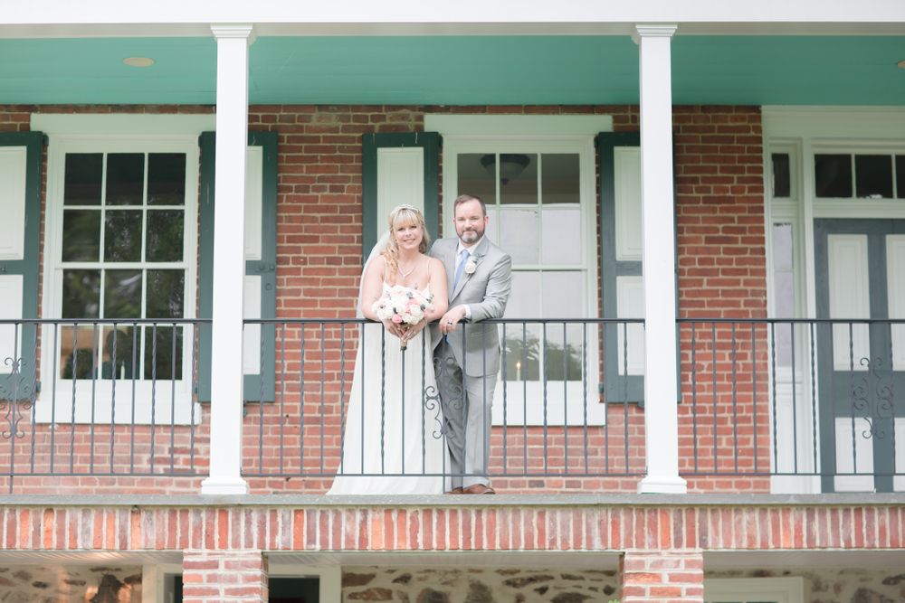 Wedding couple poses on historic brick building porch with green trim and white columns.