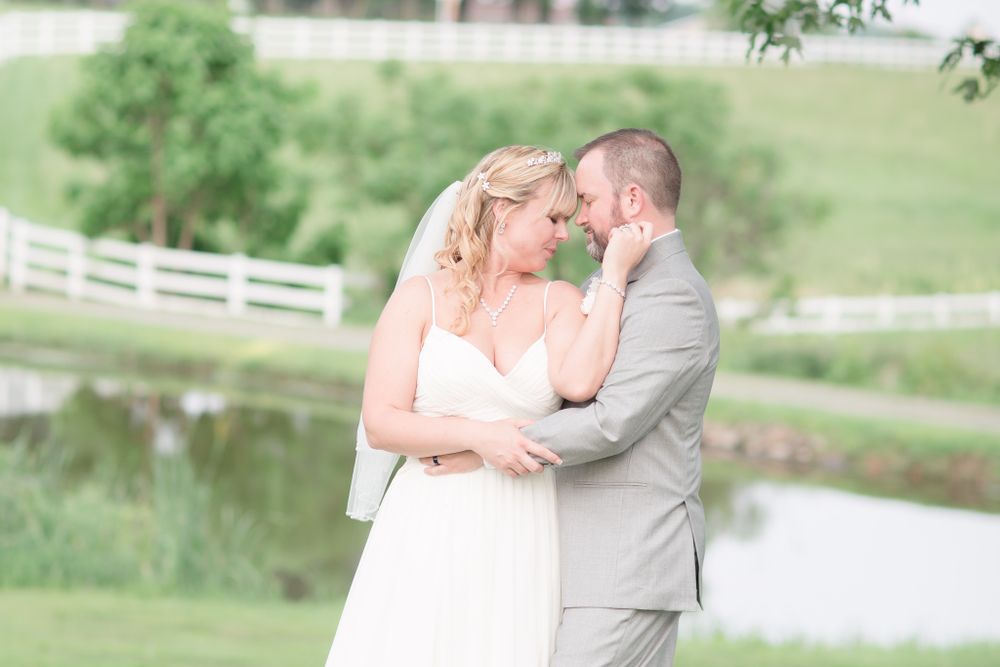 Romantic wedding portrait by a serene pond with white fencing in the background.