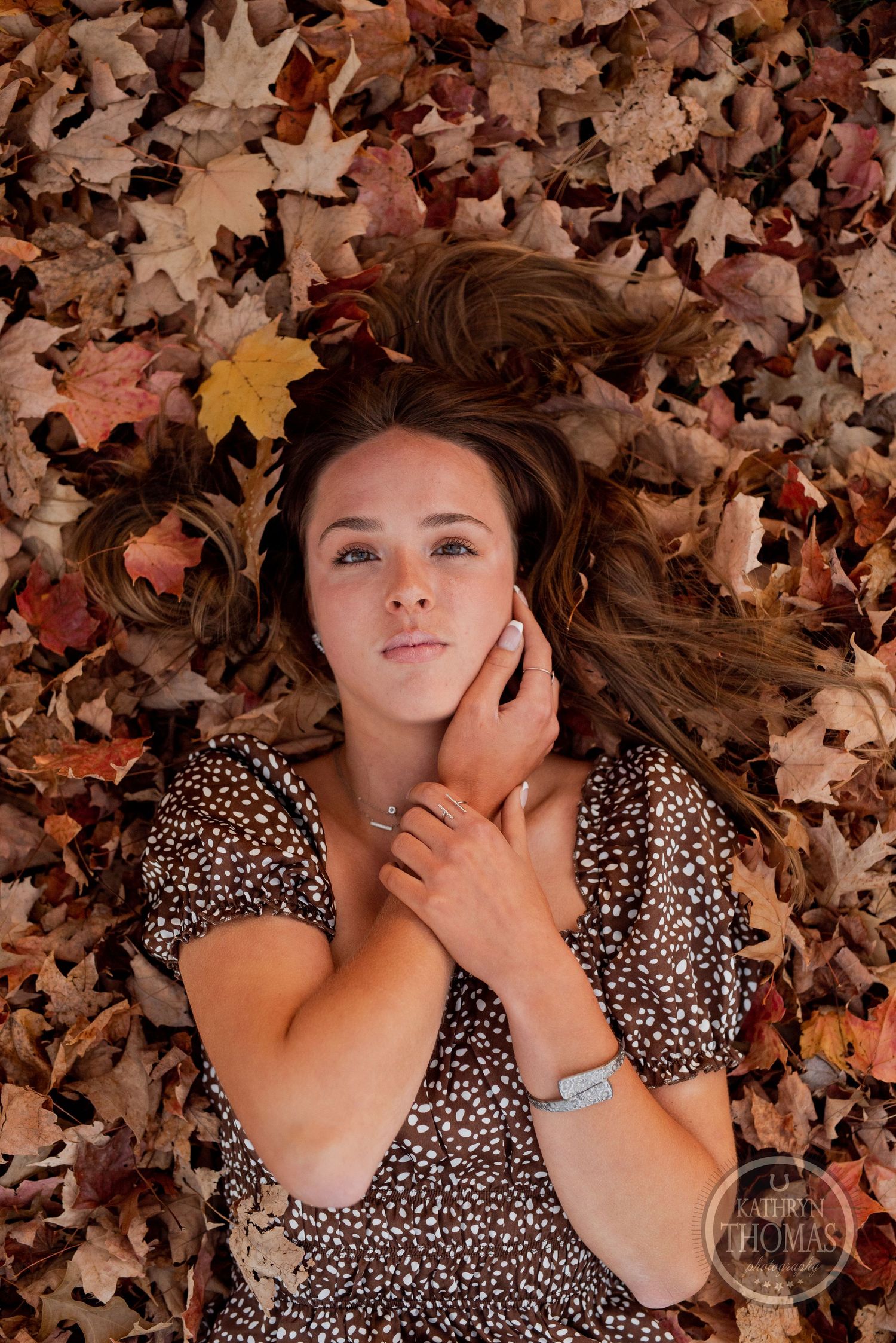 Overhead portrait of someone lying in colorful autumn leaves wearing a floral print top.