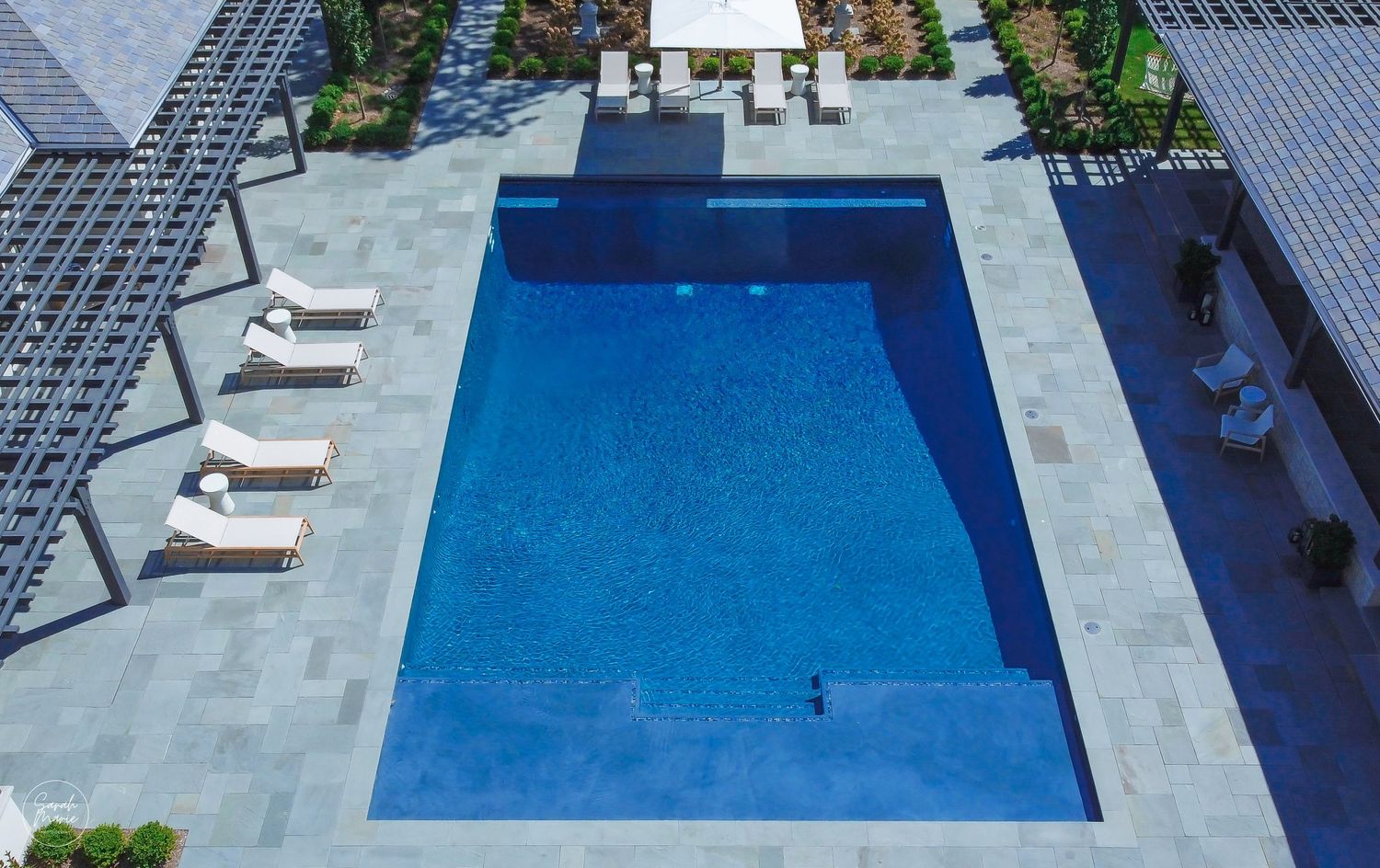 Aerial view of a modern rectangular swimming pool with lounge chairs and landscaping.