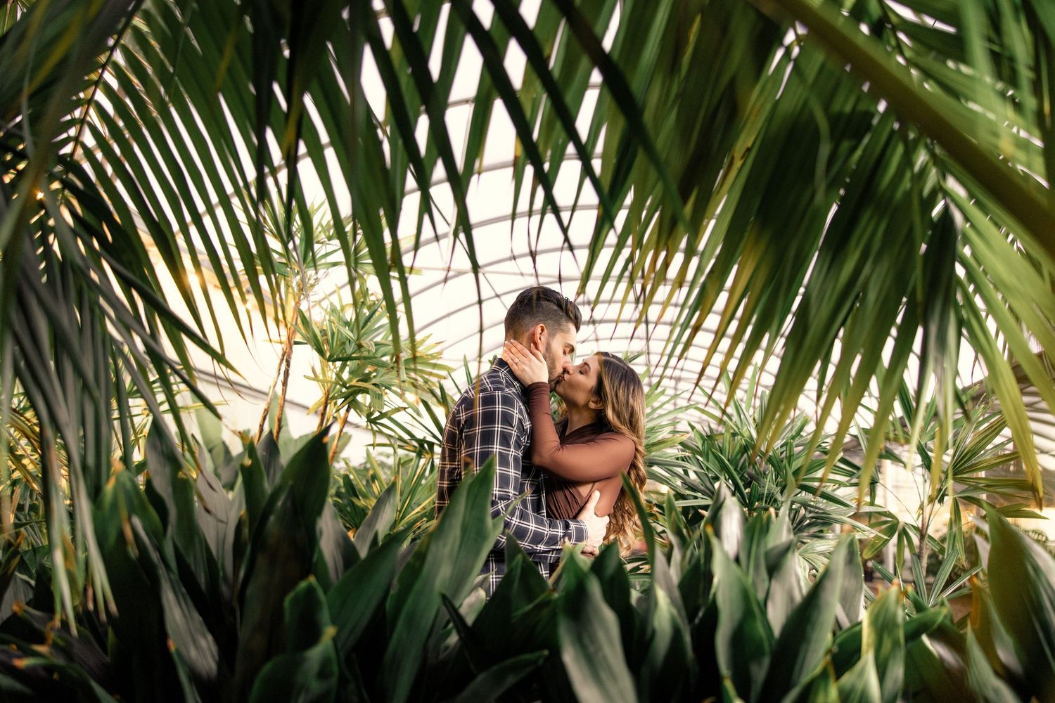 An intimate moment framed by lush tropical palm fronds and greenery in natural lighting.