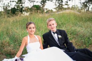 Wedding couple relaxing on grassy hillside in formal attire.