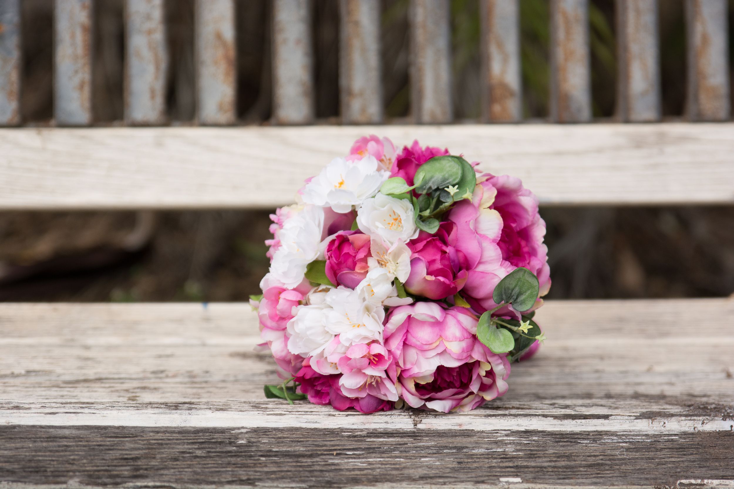 Pink and white bridal bouquet resting on weathered wooden surface.