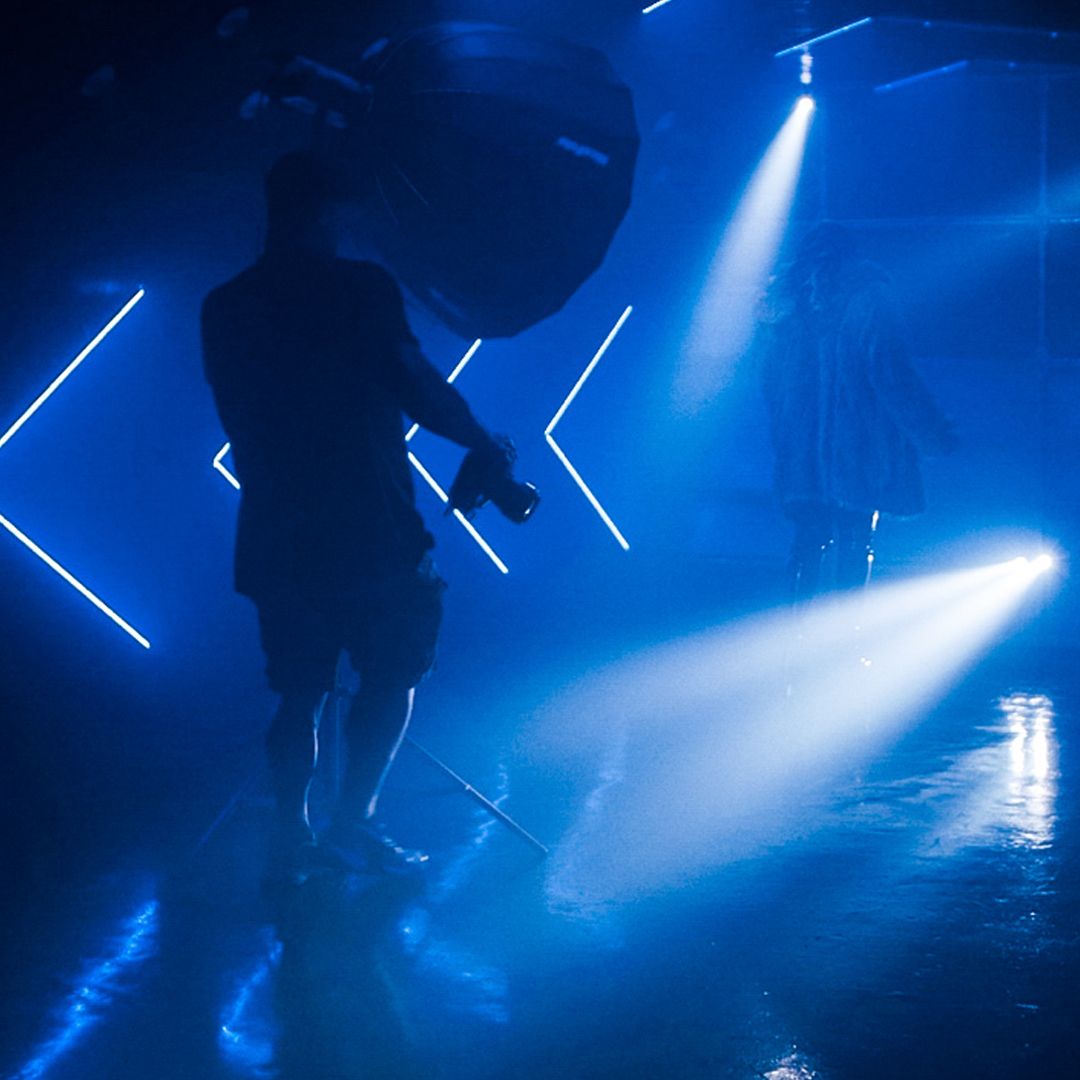 Silhouetted figure in blue-lit nightclub with geometric light patterns.