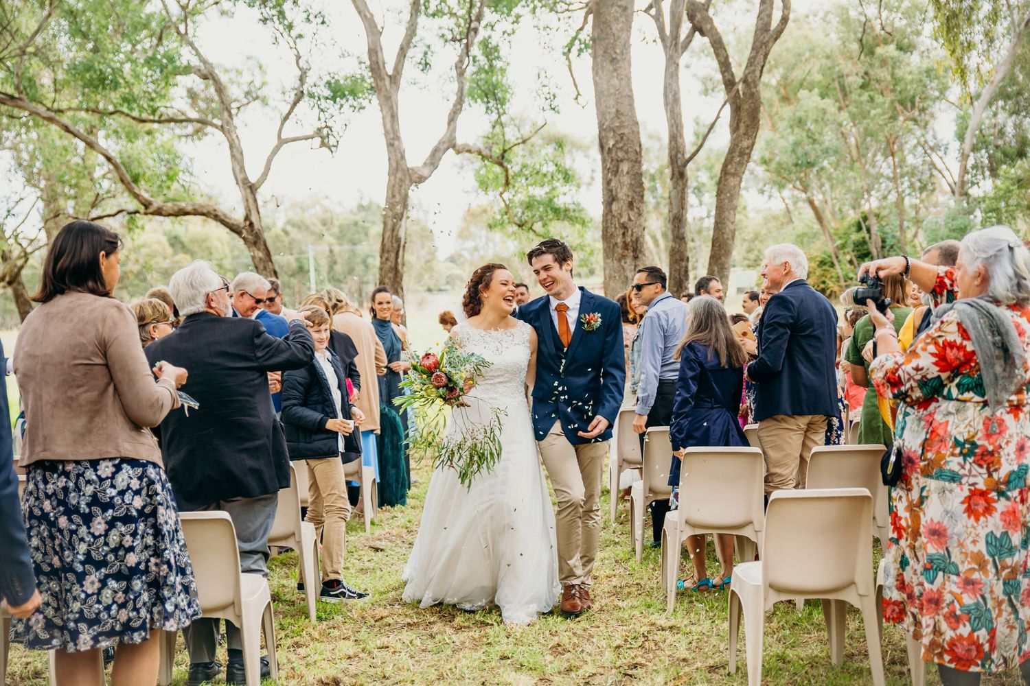 Bride and groom walk down the aisle at an outdoor wedding ceremony surrounded by guests and eucalyptus trees.