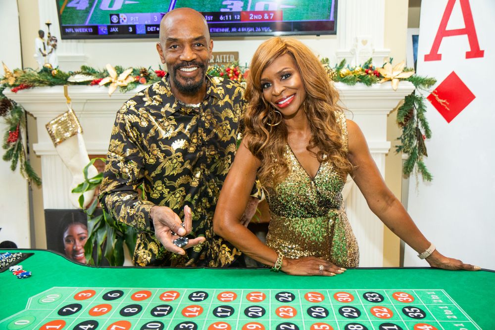 Two people enjoying a festive casino night with a roulette table decorated with holiday garland.