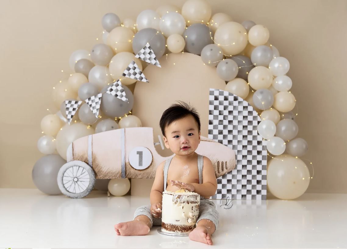 Racing themed birthday setup with checkered flags and neutral balloon arch.