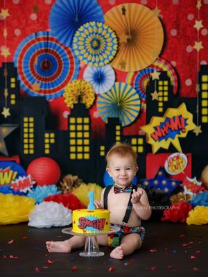Superhero cityscape backdrop with colorful paper fans and star decorations against red background.