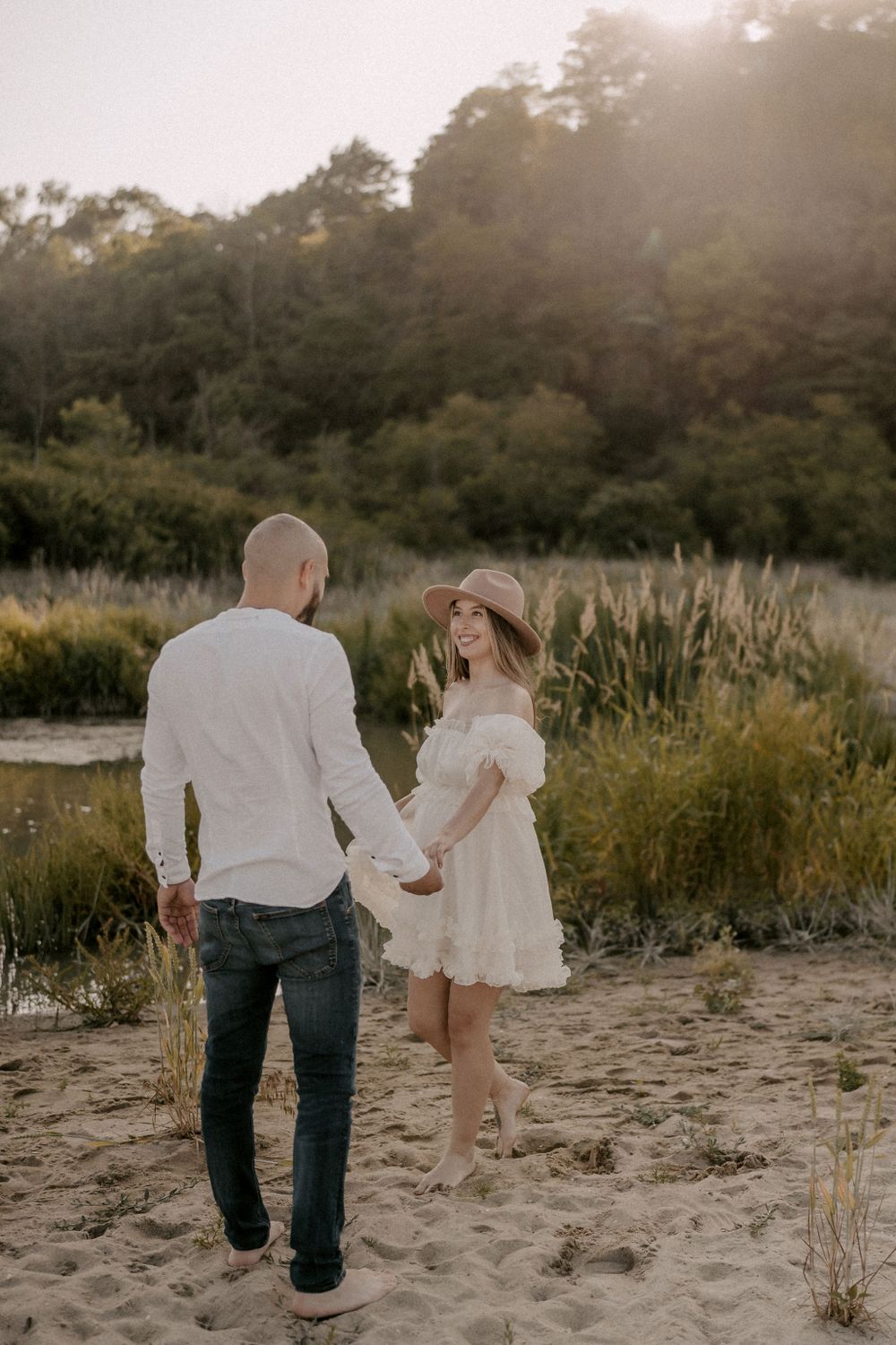 A romantic couple strolls hand in hand along a beach path at sunset.