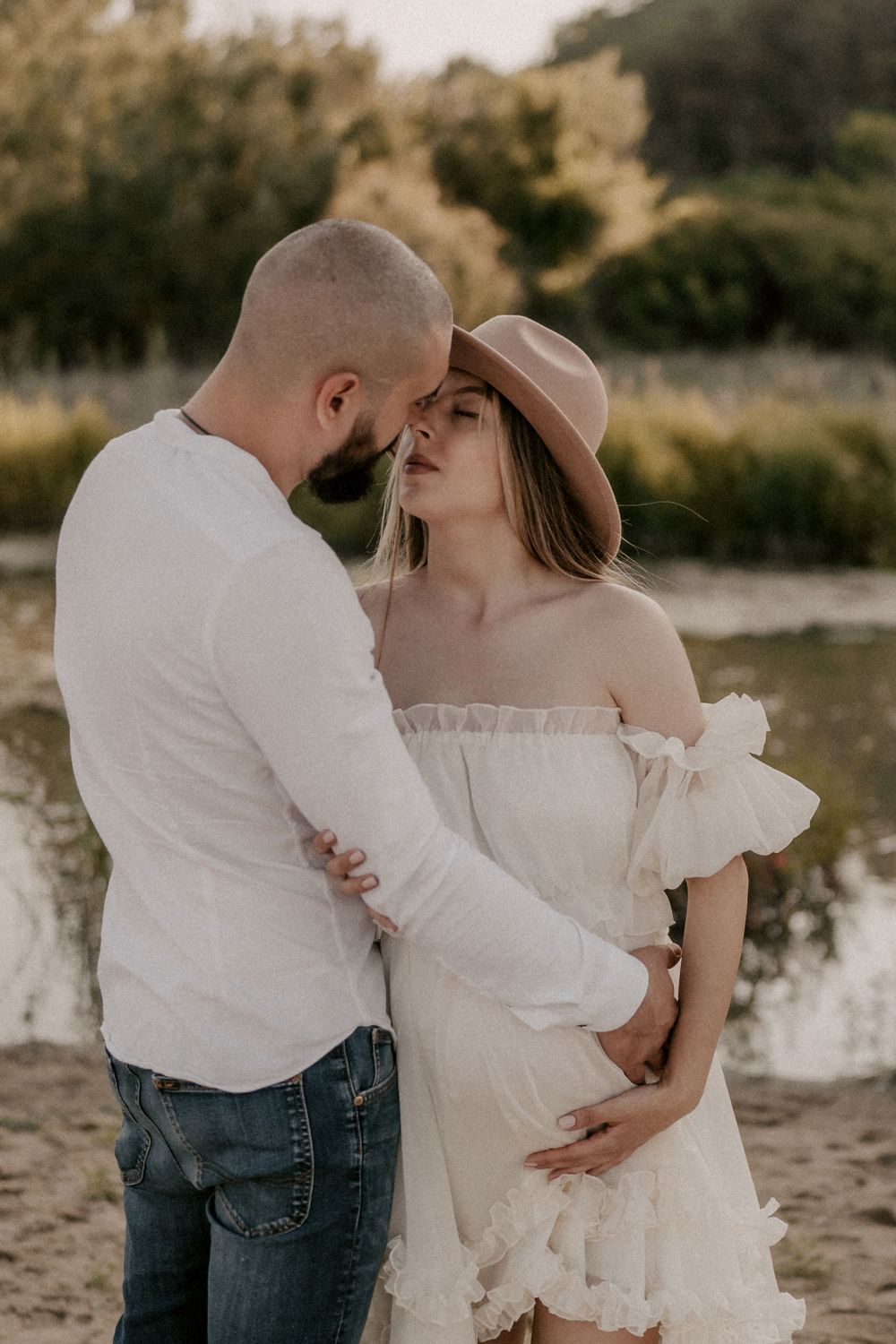 A tender moment between a couple in white and denim on a sandy beach.