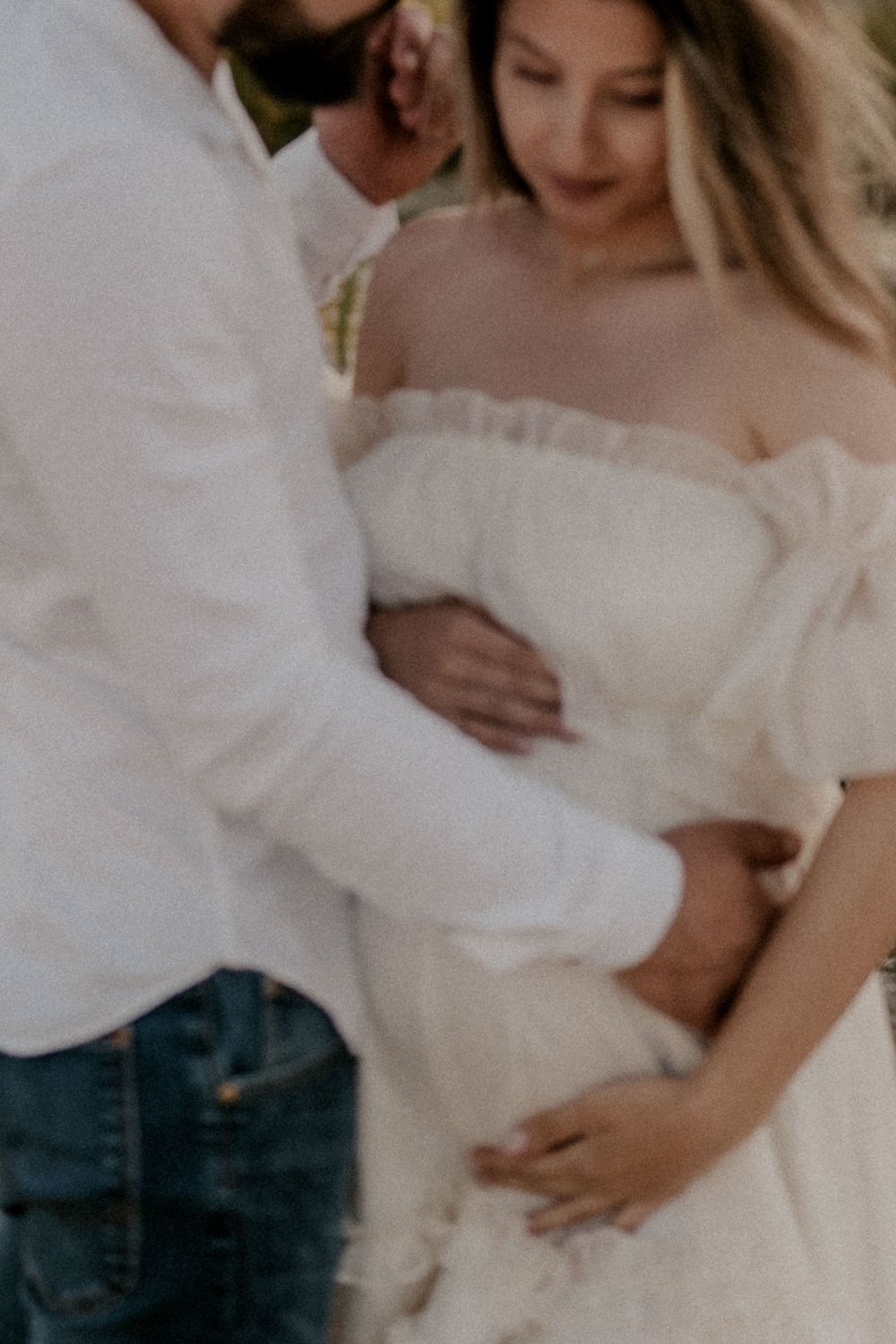 A close-up romantic moment between a couple in white attire on the beach.