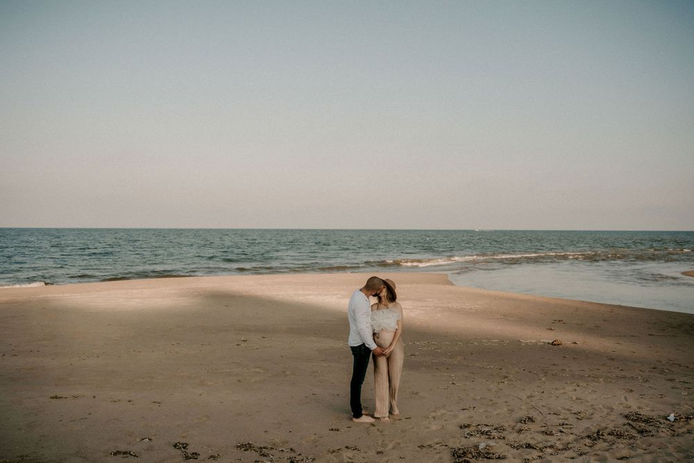 Wide angle beach landscape showing couple walking along shoreline at sunset.