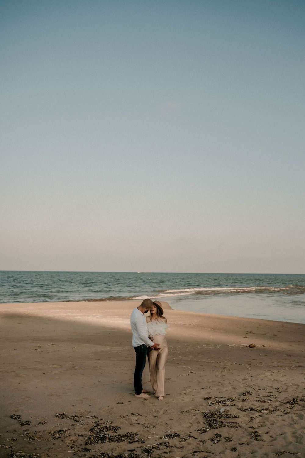 A romantic couple embraces on a serene beach at sunset with waves crashing in the background.