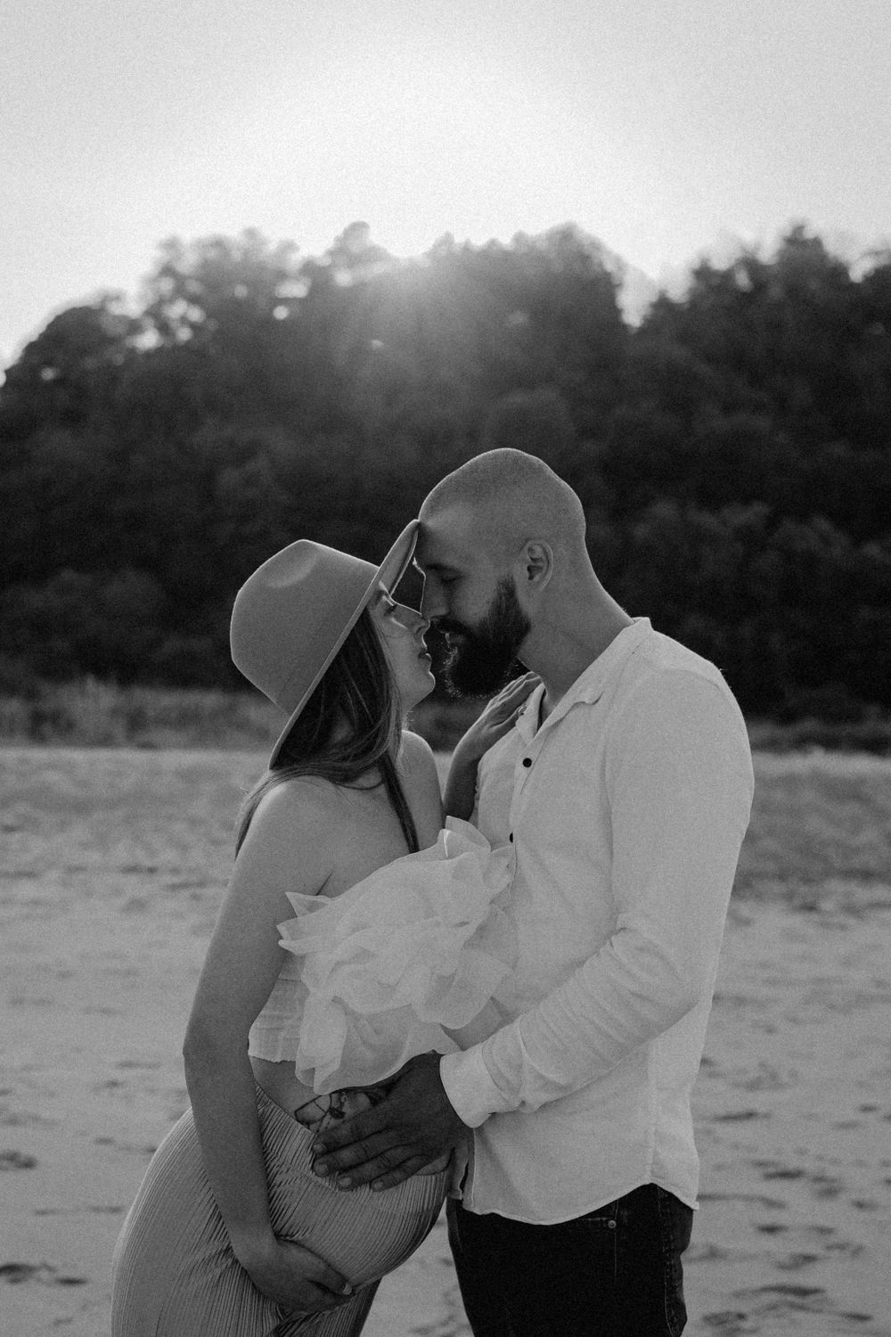 An intimate black and white portrait of a couple sharing a tender moment on the beach.