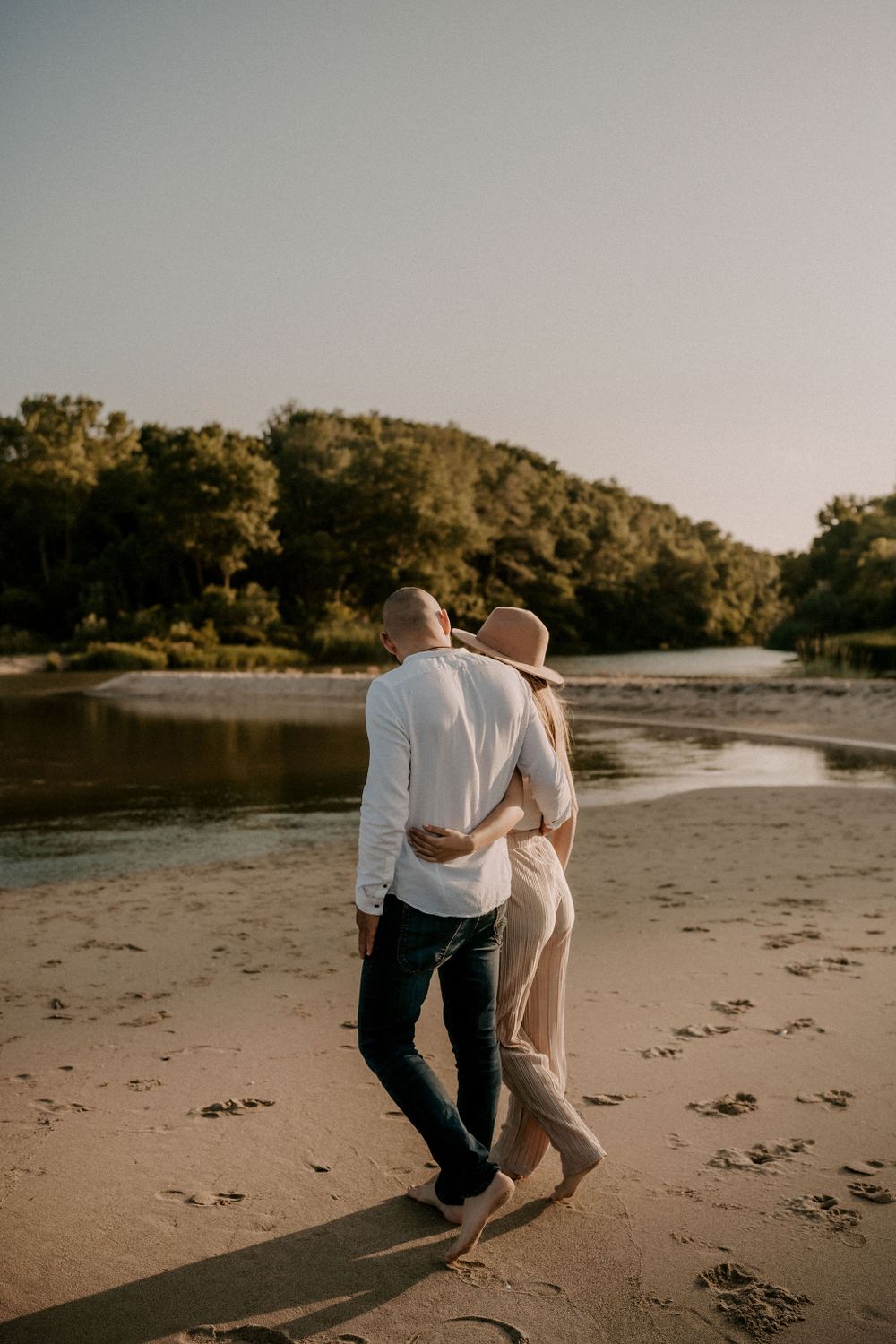 A couple walks together along a peaceful beach shoreline during sunset.