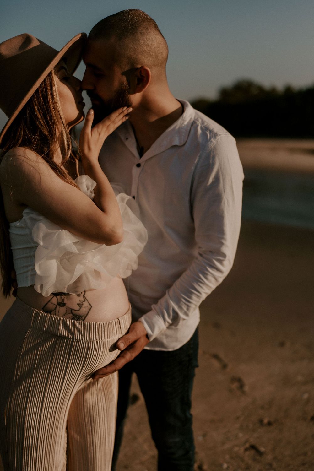 A couple shares an intimate moment on the beach during golden hour.