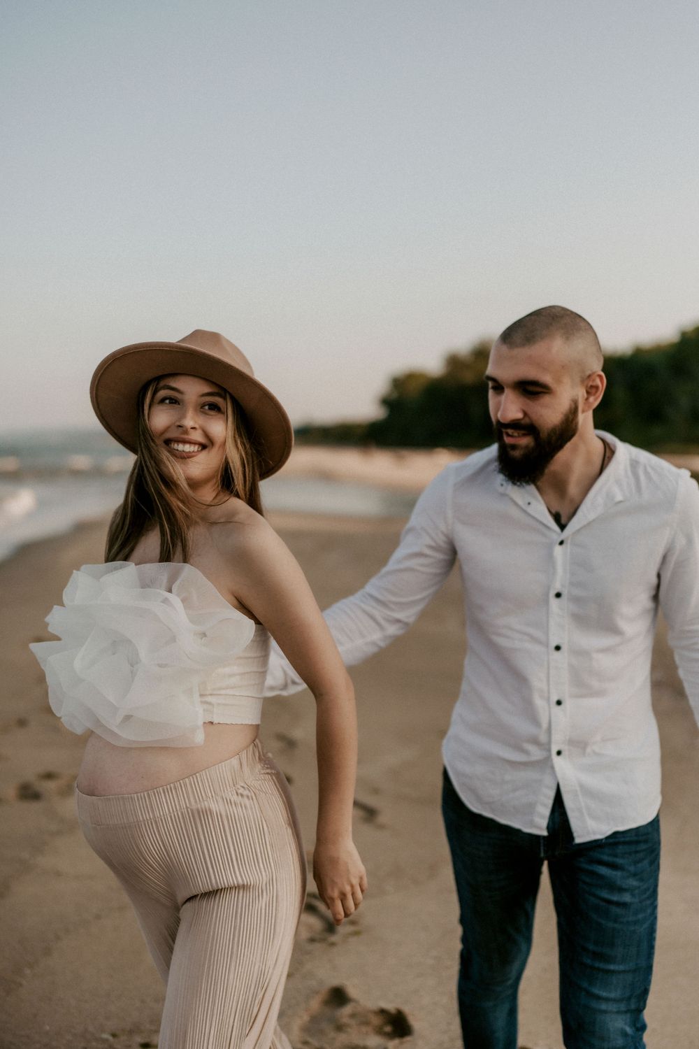 A couple enjoys a playful moment while walking on the beach at sunset.