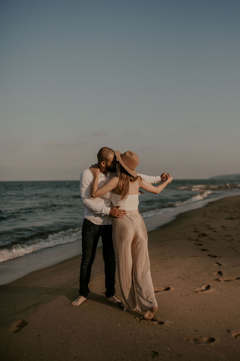 A couple dances together on the beach during golden hour with waves crashing behind them.