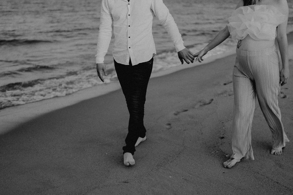 A couple walks hand in hand along a serene beach at sunset.